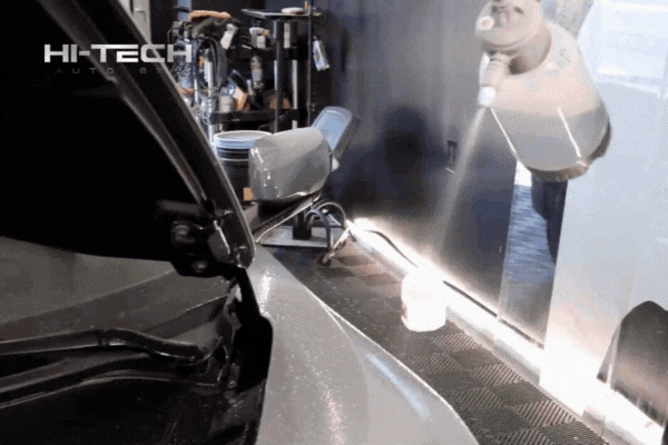 GIF showing a Hi-Tech Auto Spa technician spraying liquid over a car panel in a professional detailing bay. The scene highlights the careful, controlled process of prepping a vehicle for paint protection film installation.
