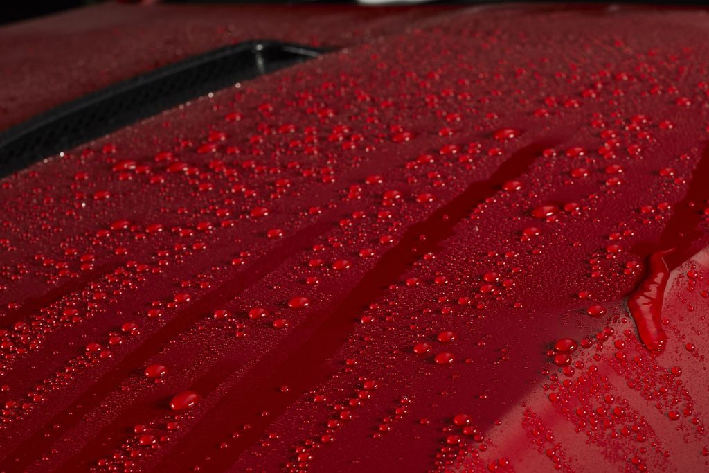 Close-up of water beading on a glossy red car surface, showing the hydrophobic finish created by ceramic coating ingredients like SiO₂ and PDMS polymers.