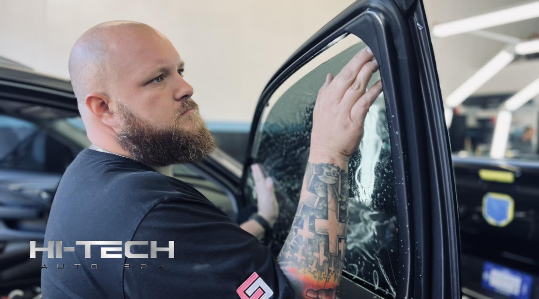 A bearded technician at Hi-Tech Auto Spa in Savannah, GA carefully applies window tint film to a car door window, showcasing the hands-on process and precision involved in professional tinting. This visual highlights the practical Benefits of Window Tinting in a sunny coastal city.